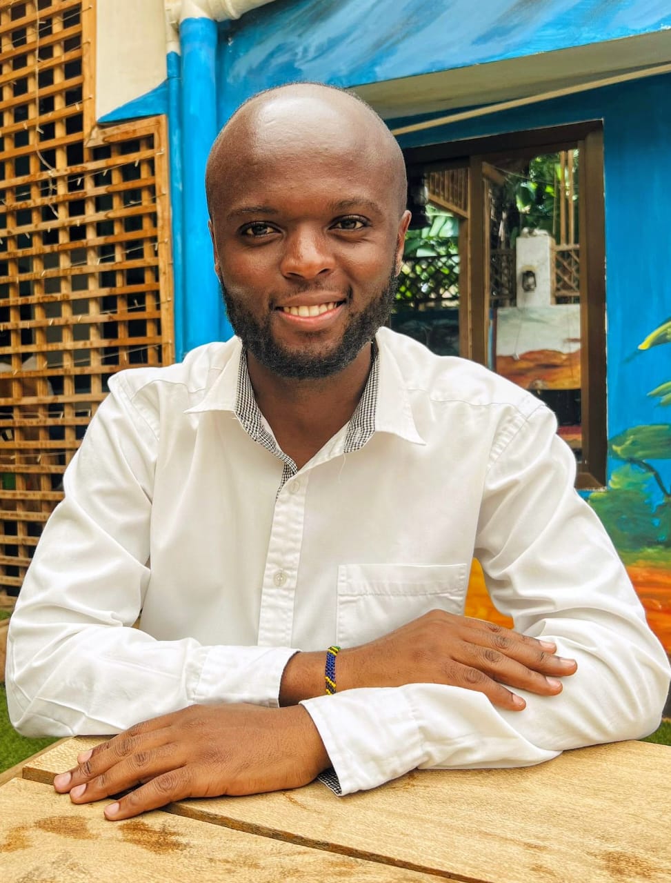 Boniphace Maruchu smiling while seated at a wooden table
